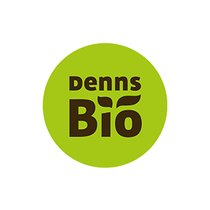 Logo von Denns Bio mit grünem kreisförmigen Hintergrund. Das Wort Denns erscheint über Bio, mit zwei grünen Blattformen über dem i in Bio, als Symbol für organische oder natürliche Produkte.