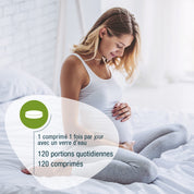 Eine schwangere Frau lächelt auf einem Bett und berührt ihren Bauch. Französischer Text mit Dosierungsangaben für gse.organic.supplements Folsäure Compact (Bio) FR: 120 Tagesportionen, 120 Tabletten-perfekt zur Unterstützung der Folsäure Schwangerschaft.