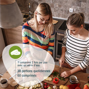 Zwei Frauen schnippeln Gemüse in einer Küche. Eine französische Infografik zeigt VeganPlus (Bio) FR von gse.organic.supplements: 1 comprimé 2x/jour avec un verre d'eau, 30 portions par flacon, 60 comprimés pour une alimentation végane.