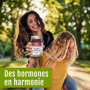 Zwei lächelnde Menschen befinden sich im Freien; einer trägt den anderen auf dem Rücken und hält dabei ein Glas „Confort menstruel (bio)“ von gse organic supplements in der Hand. Sonnenlicht fällt durch die grünen Bäume und schafft eine Atmosphäre des Wohlbefindens und des hormonellen Gleichgewichts. Der französische Text lautet: „Des hormones en harmonie.“.