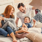 Eine fröhliche vierköpfige Familie im Pyjama lacht und spielt auf einem sonnenbeschienenen Bett – und strahlt das Wohlbefinden aus, das CitroPlus® 1200 forte (Bio) von gse.organic.supplements bietet, während sie diesen glücklichen, entspannten Moment zusammen genießt.